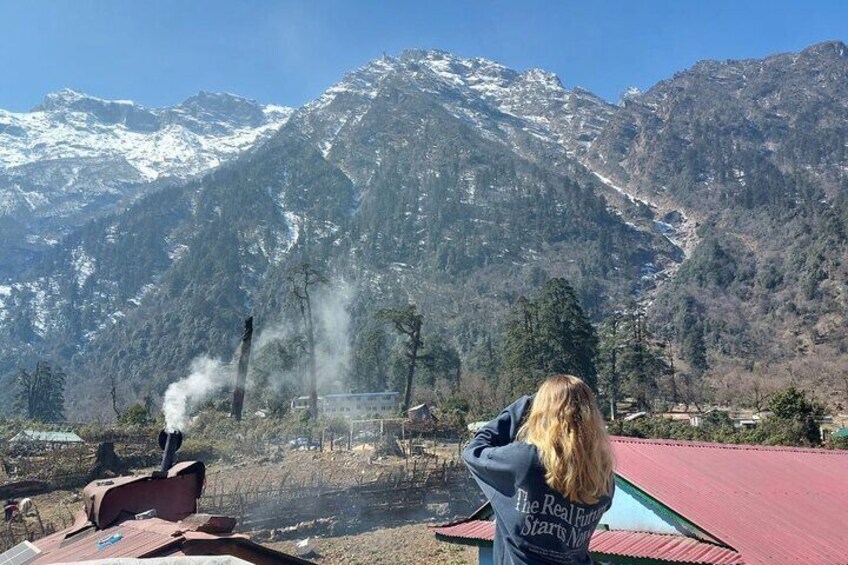 A person taking a photo of a steam locomotive in a mountainous area with snow-capped peaks in the background. 3
