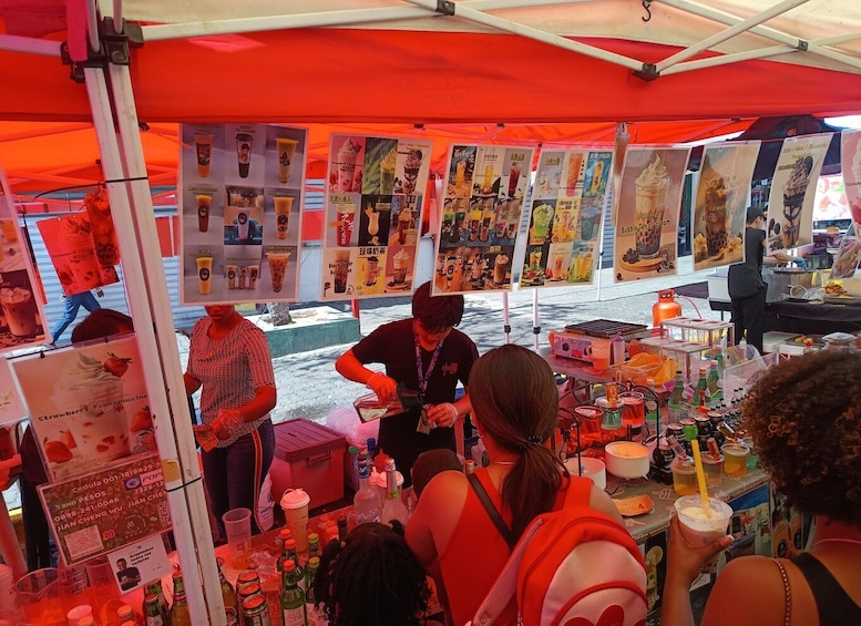 A street food stall with a variety of colorful drinks and a menu board displaying different beverage options. 2