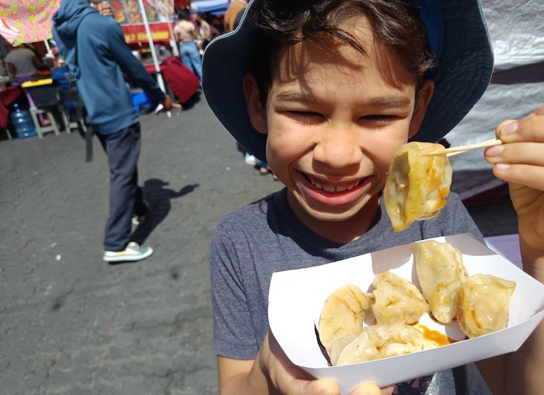 A person holding a box of food items, likely street food, with a crowd in the background. 1