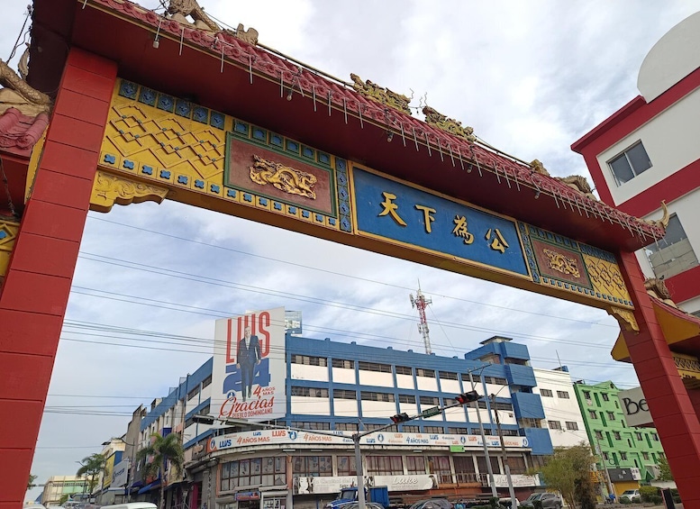 A colorful archway with Chinese characters, a building with a blue and white facade, and a billboard advertising a Dominican event. 5