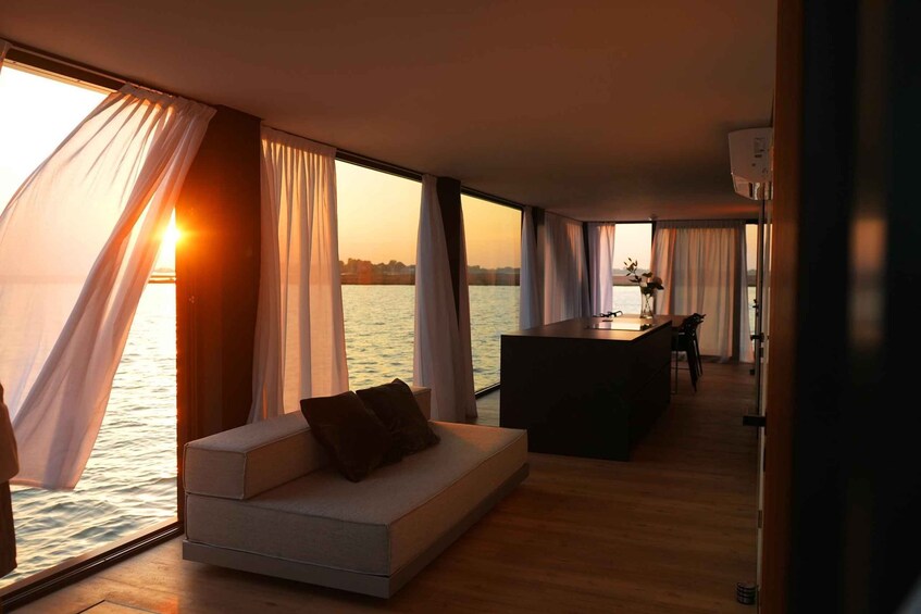 A modern interior with a sofa, dining area, and large windows overlooking a body of water. 4