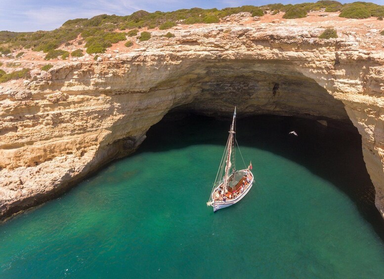 A sailboat anchored in a natural cave opening surrounded by rocky terrain. 4