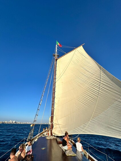 A sailboat with a large sail, passengers on deck, and a clear blue sky. 3