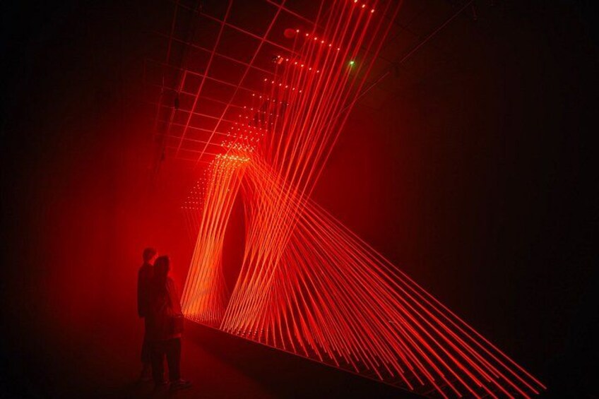 A person standing in a dimly lit area with red laser lights creating patterns on the floor. 5
