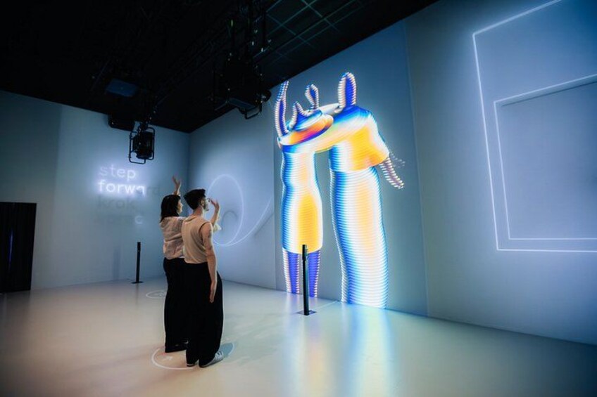 A person taking a photo of a digital art installation with two figures in blue and yellow. 3