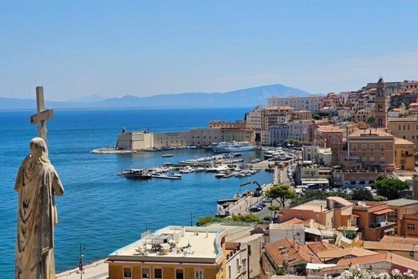 A coastal town with a prominent statue, historic buildings, and a marina with boats. 1