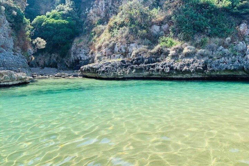 A clear coastal water body with rocky cliffs and dense greenery. 3
