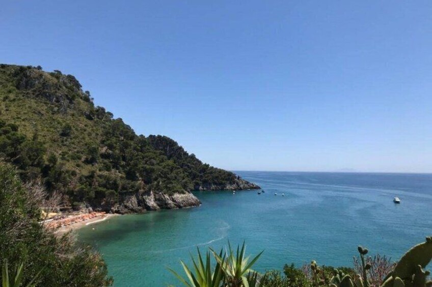 A coastal landscape with a beach, clear blue sea, and a hilly backdrop. 2
