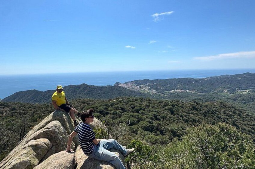 Two people sitting on a rock overlooking a mountainous landscape with a view of the ocean. 2