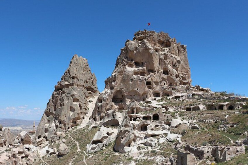 A rocky landscape with multiple cave dwellings and a flag on a peak. 4