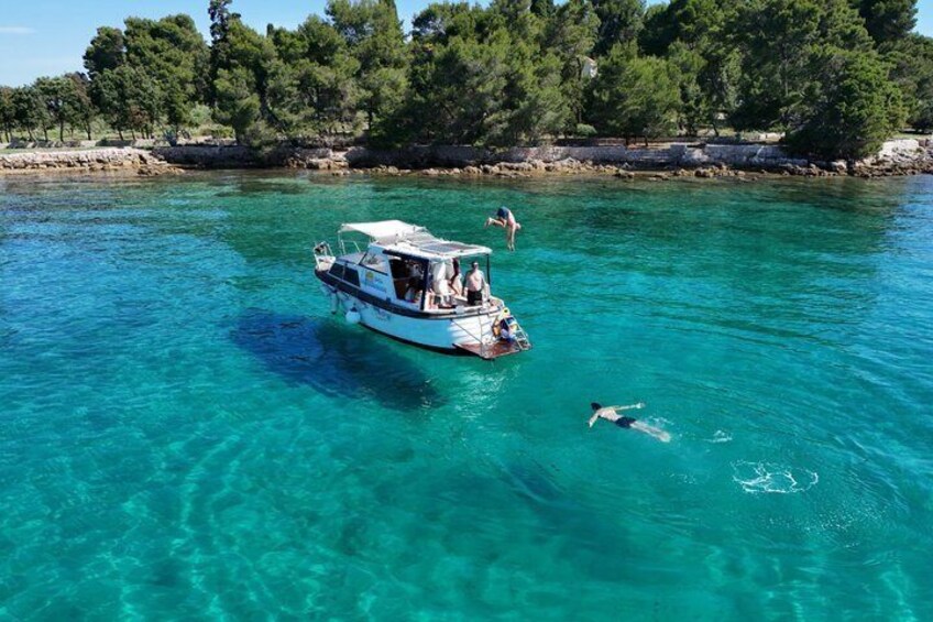 A boat on clear turquoise water with people swimming and standing on the shore. 1