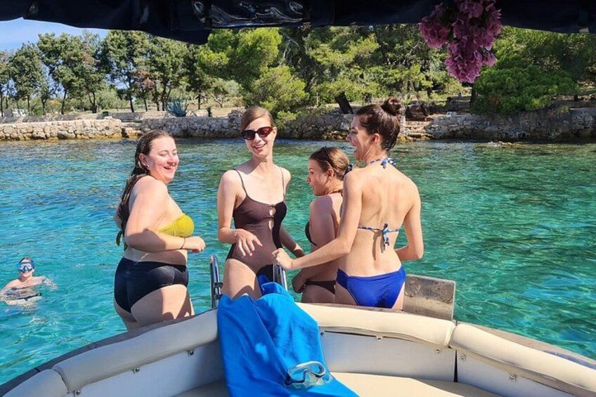 A group of people on a boat in a clear blue body of water, with a rocky shoreline and trees in the background. 3