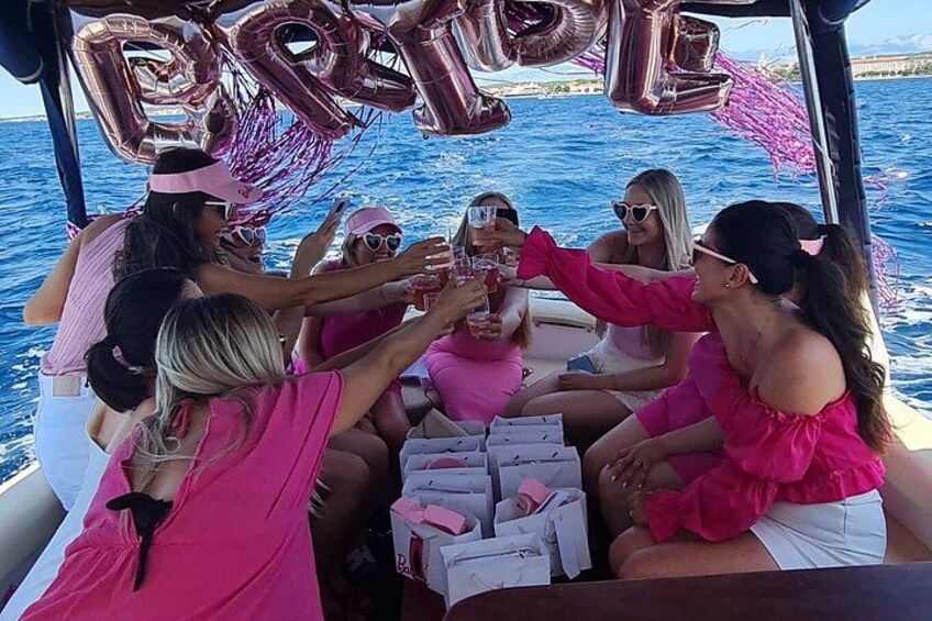 A group of people on a boat, toasting with drinks, surrounded by pink decorations and balloons. 4