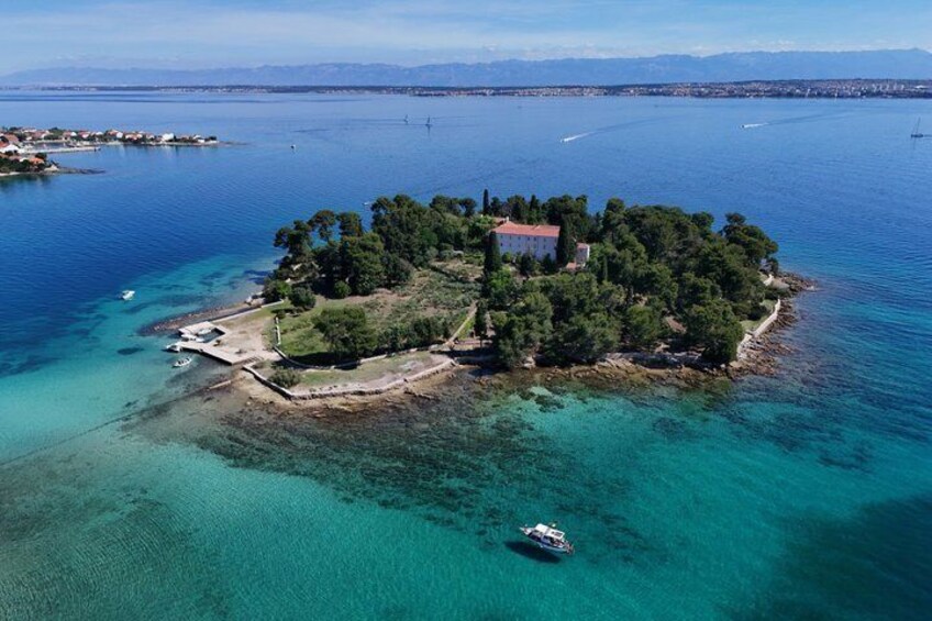 An island with a red-roofed building surrounded by trees, a small dock, and clear turquoise waters. 2