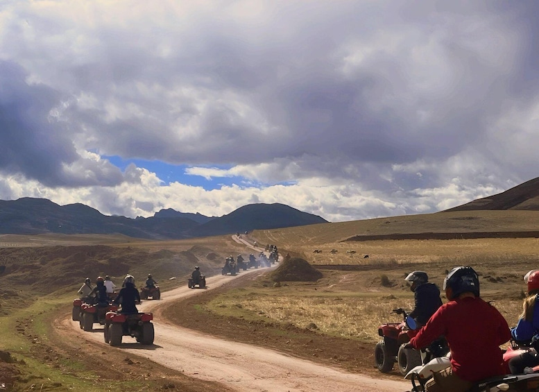 A group of riders on ATVs on a dirt road with mountains in the background. 2