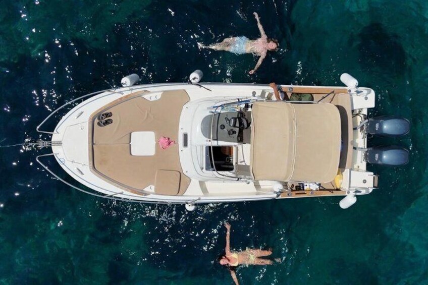 A boat with a covered deck and two people swimming in the water. 5