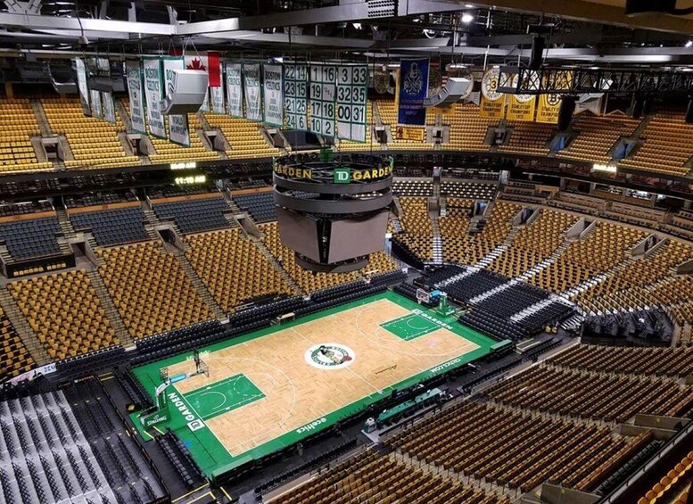 An indoor basketball court with empty spectator seats and a scoreboard. 1
