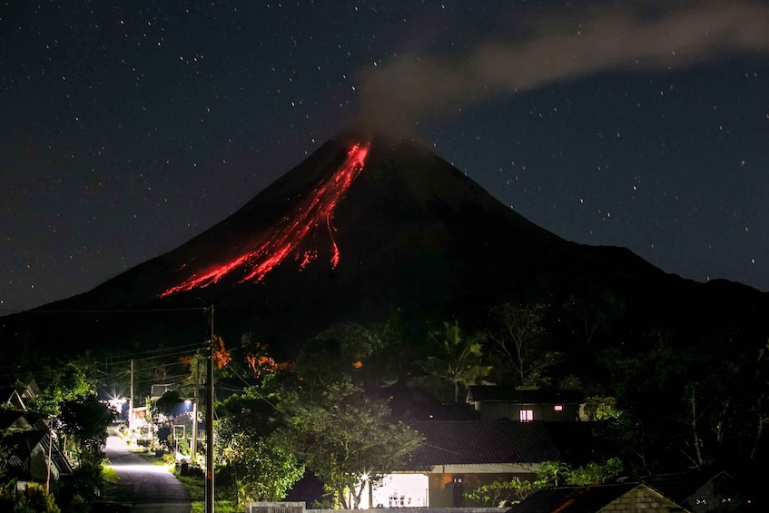 A volcano with a lava flow at night, surrounded by houses and trees. 3