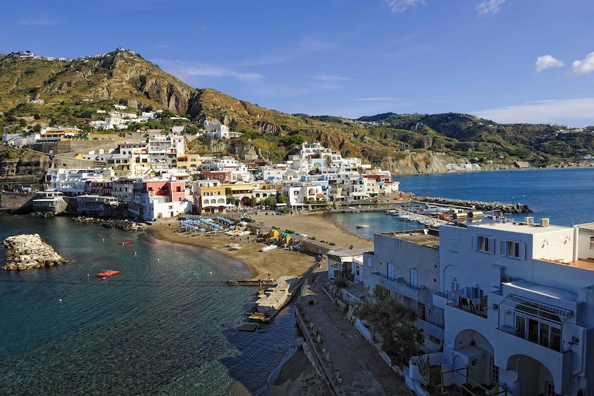 A coastal town with colorful buildings, a rocky hillside, and a marina. 2