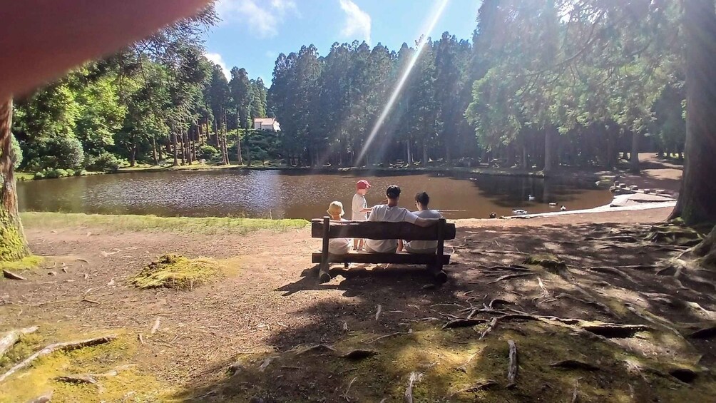 A group of people sitting on a bench overlooking a lake surrounded by trees. 5
