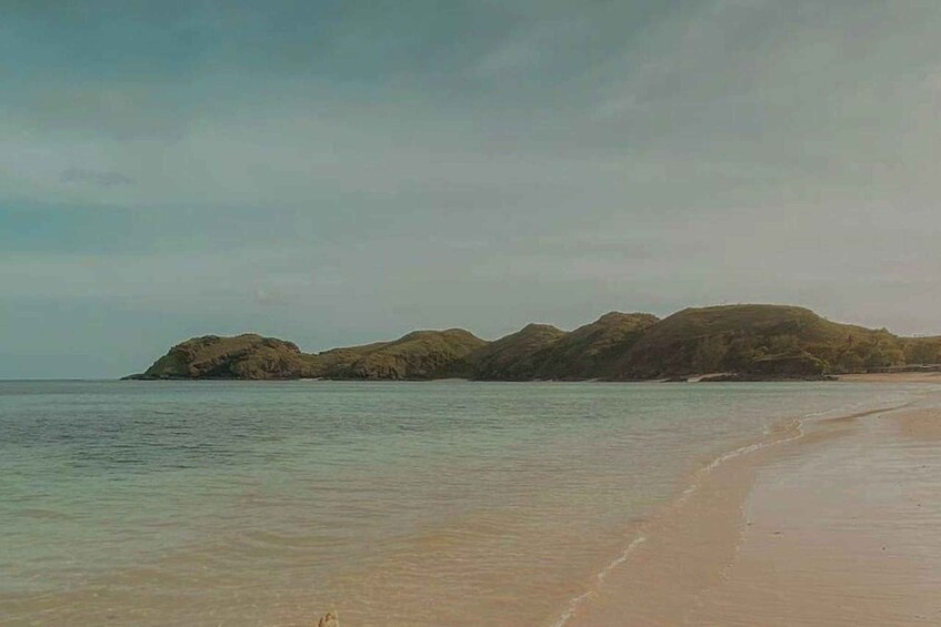 A beach with clear water and distant rocky outcrops. 4