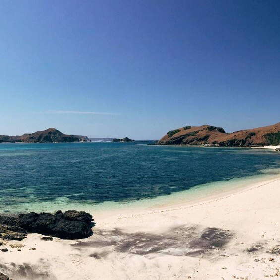 A beach with clear turquoise water, sandy shore, and rocky outcrops. 2