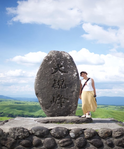 A person standing next to a large stone with inscriptions, overlooking a green valley. 2