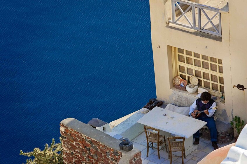 A person playing guitar on a balcony overlooking a blue sea. 4