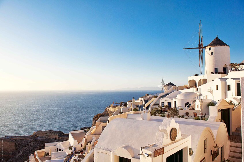 A coastal village with white-washed buildings, a windmill, and the sea in the background. 1
