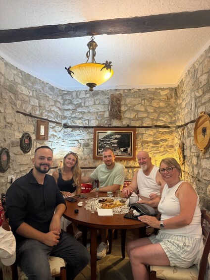 A group of people seated around a wooden table in a stone-walled room with a hanging lamp. 3