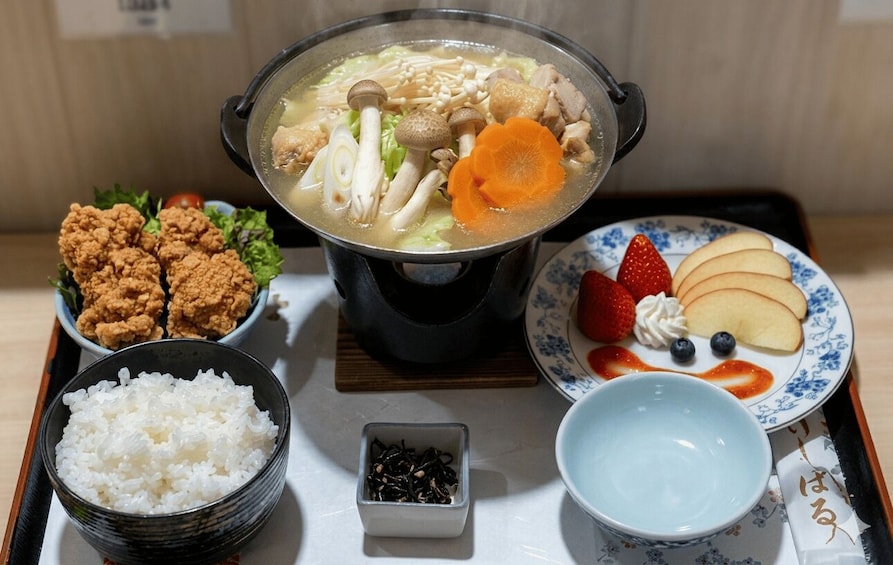A traditional Japanese meal with a pot of soup, fried chicken, rice, and a plate with fruit and cream. 5