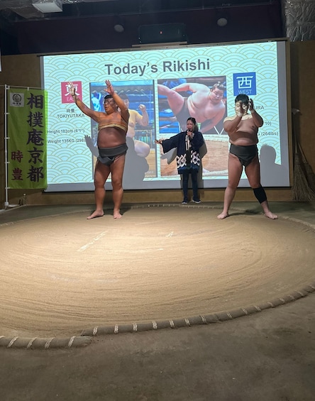 A stage with three individuals, one holding a microphone, and a backdrop with text and images. 4