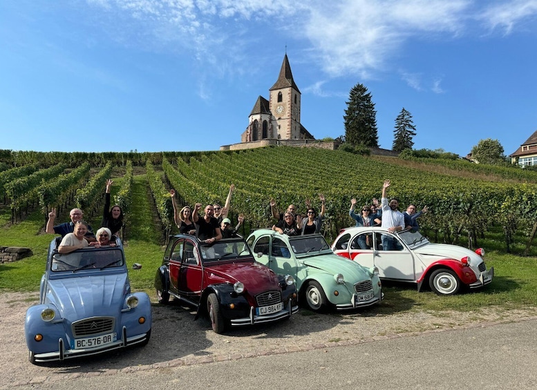 Vintage cars parked on a gravel road with a church and vineyard in the background. 5