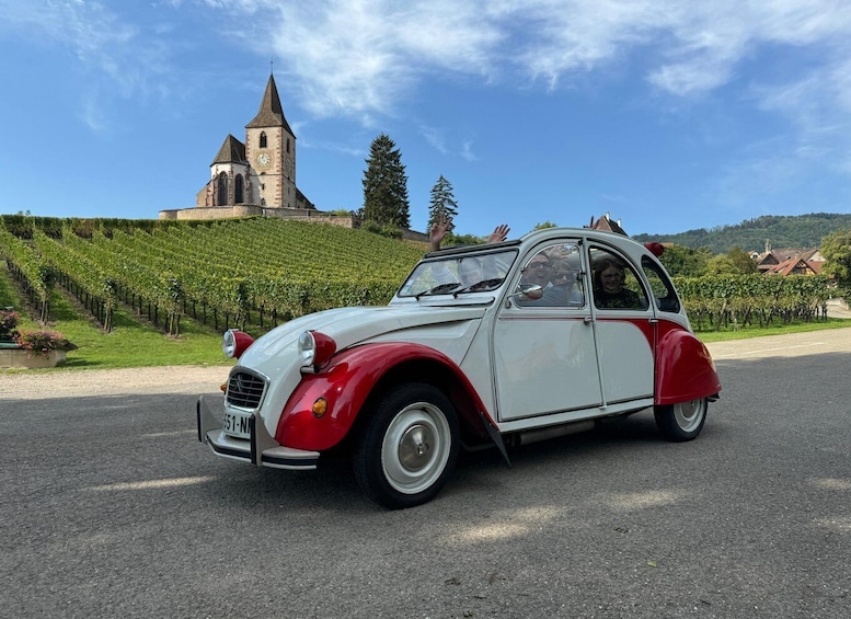 A vintage car parked on a road with a church and vineyard in the background. 3