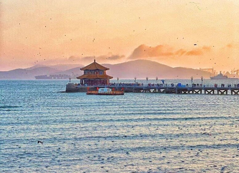 A traditional pavilion on a pier extending into the water, with a mountainous backdrop and a clear sky. 4