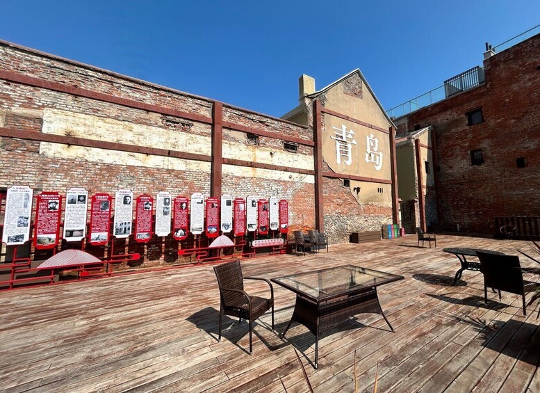 An outdoor seating area with tables and chairs, a brick wall with informational signs, and a building with Chinese characters. 3
