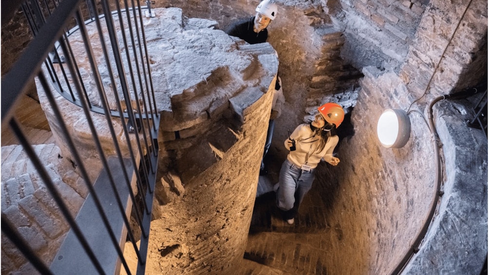 A person in a helmet and safety gear inside a stone-lined tunnel with metal railings. 4