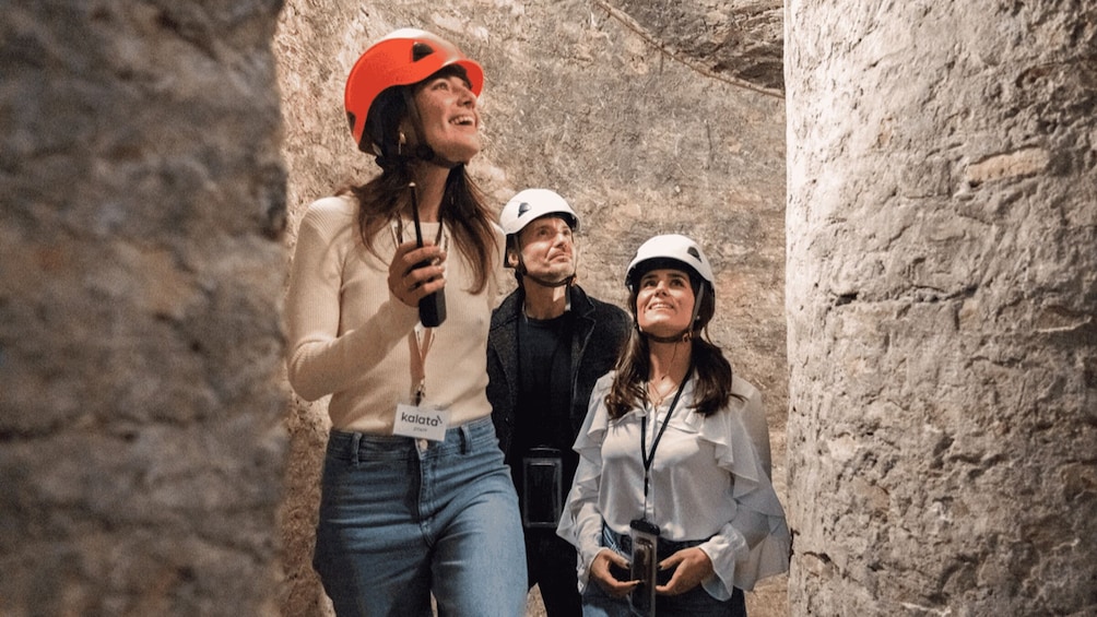 Three people in a rocky cave environment, wearing helmets and casual clothing. 1