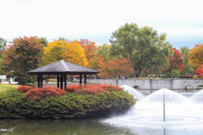 A gazebo by a pond with a bridge in the background and autumn foliage. 5