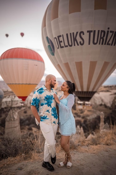 A couple standing in a rocky landscape with hot air balloons in the background. 3