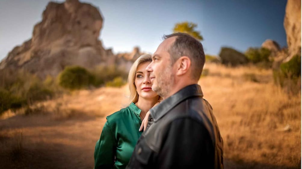A couple standing in a desert landscape with a large rock formation in the background. 5