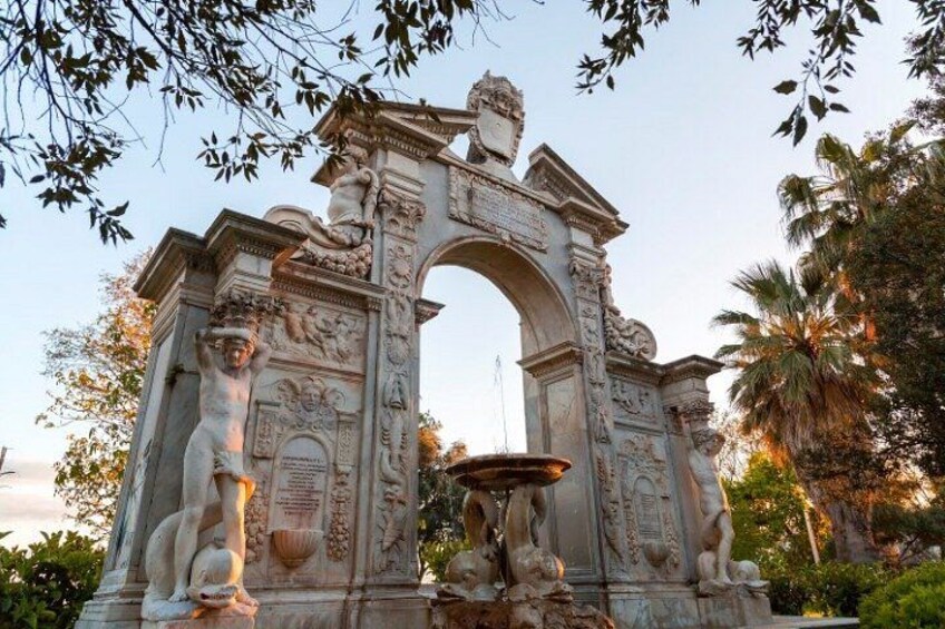 An ornate stone archway with sculptures and inscriptions, surrounded by greenery. 5