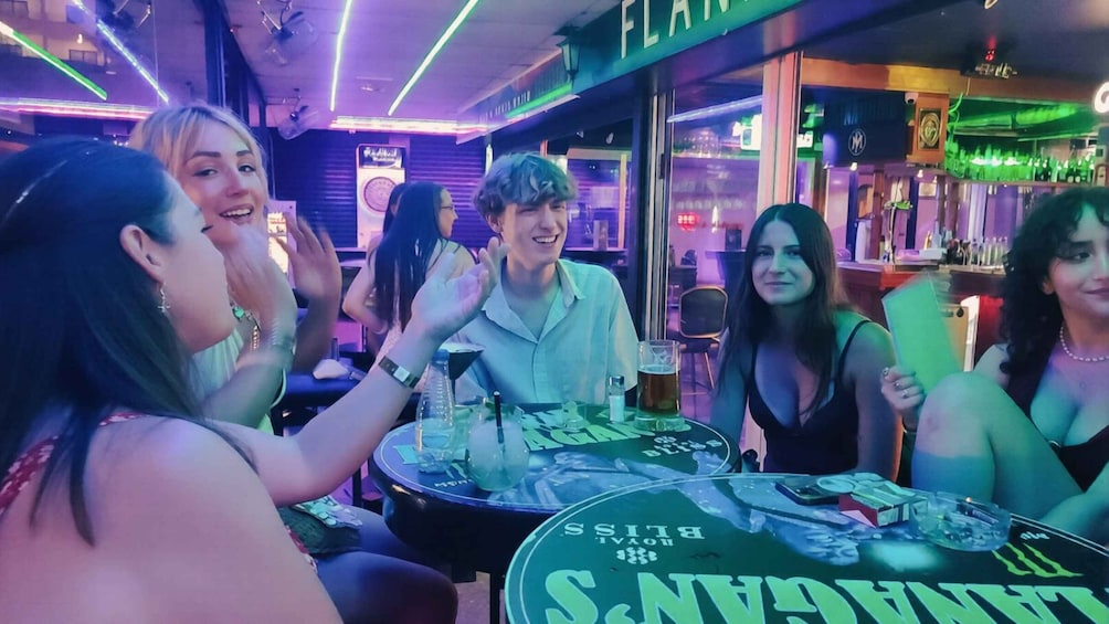 A group of people at a bar with neon lights and a sign that reads 'FLAMINGOS.' 1