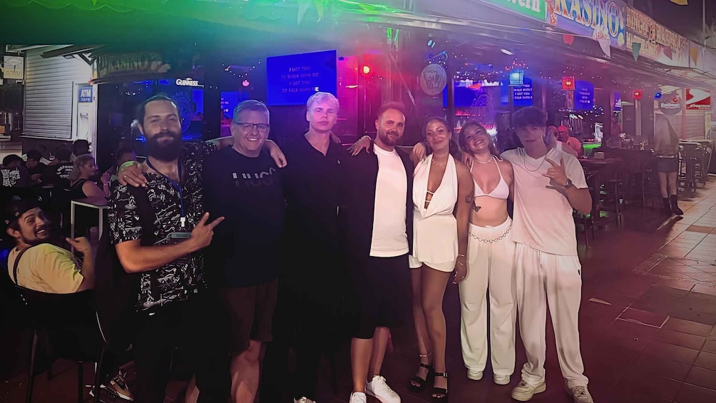 A group of people posing in a bar with neon signs and a dance floor in the background. 2