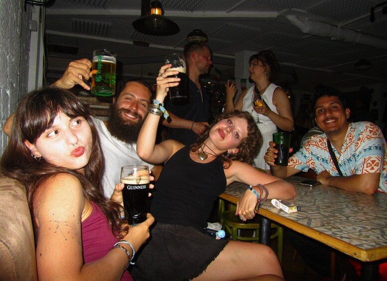 A group of people sitting at a table, holding drinks, in a dimly lit indoor setting. 5