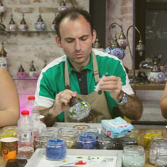 A person in a green shirt and apron working with colorful beads and small jars on a table. 5