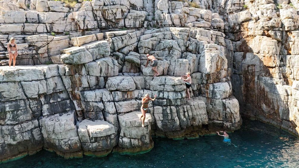 People climbing a rocky cliff by a body of water. 5