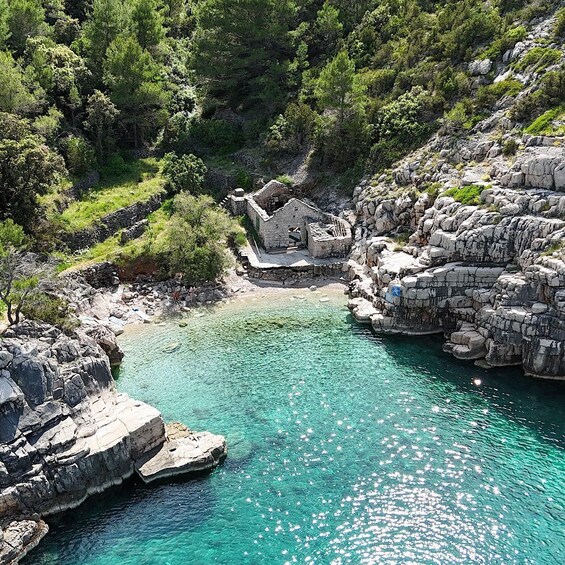 A coastal landscape with clear turquoise waters, rocky cliffs, and a small stone building near the shore. 5