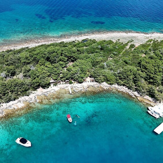 An aerial view of a turquoise coastal area with boats, a rocky shoreline, and dense green vegetation. 4