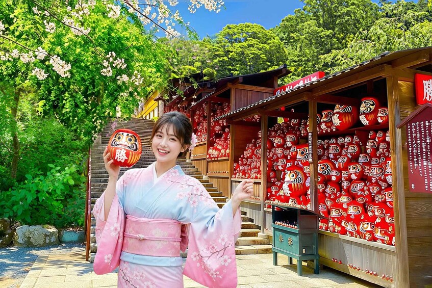 A person in traditional attire holding a decorative item, with cherry blossoms and a shrine in the background. 1